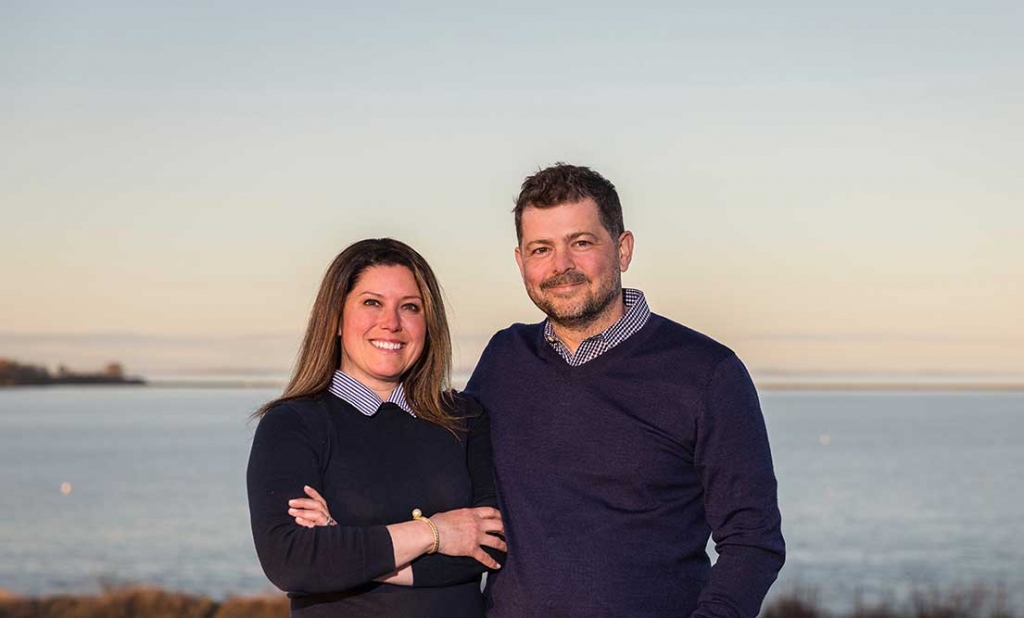 A portrait of City + Harbor Real Estate Group Agents Fletcher and Michael with the Maine coast in the background.